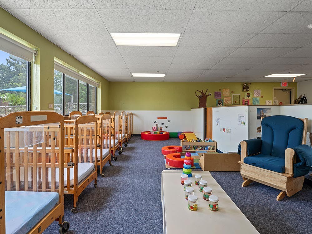 cribs in a daycare room with a rocking chair and toys