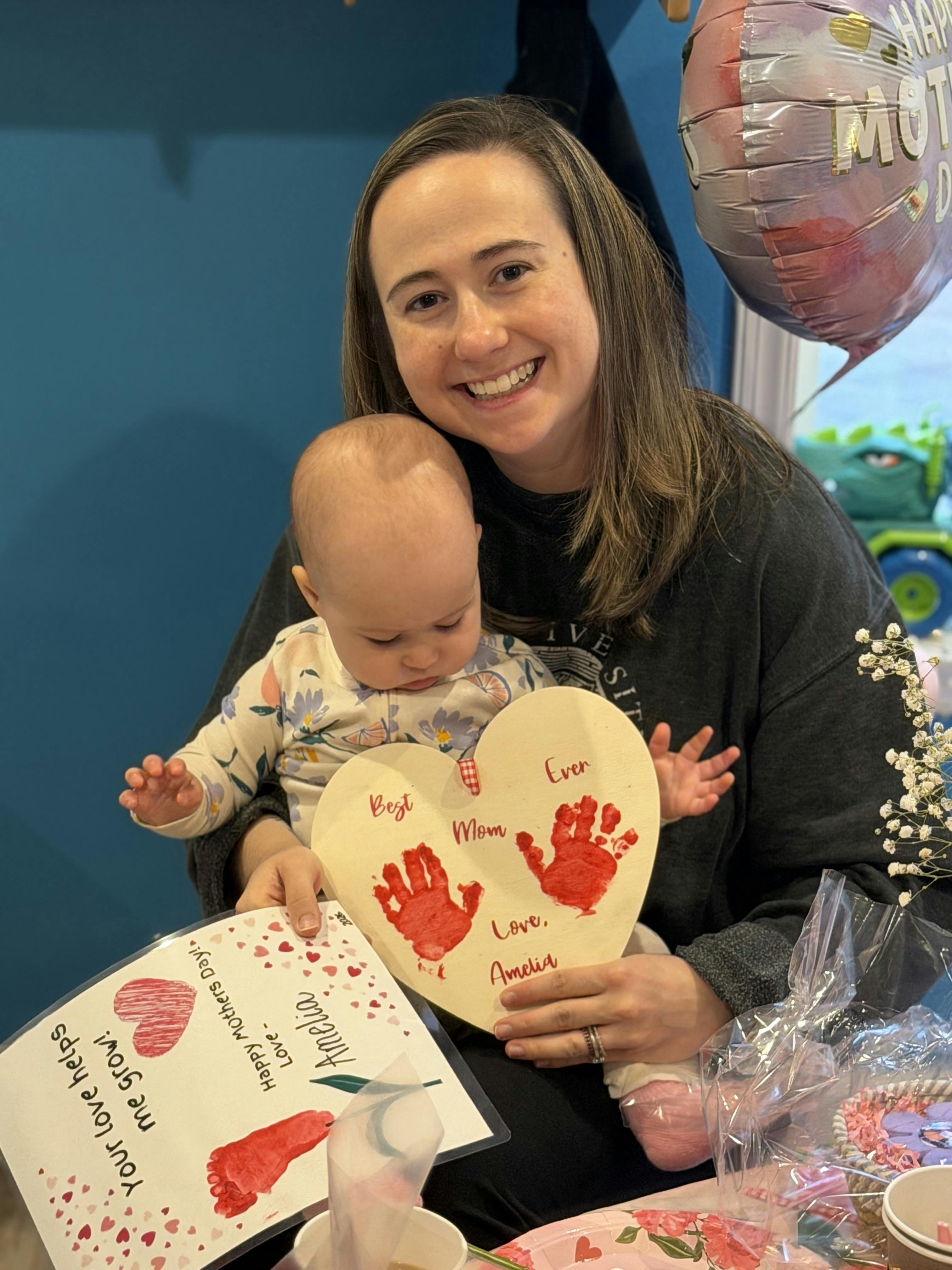 Person holding a child and a heart-shaped sign with red handprints and text