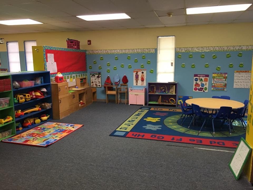 Classroom with colorful rugs, shelves of toys, and a round table with chairs