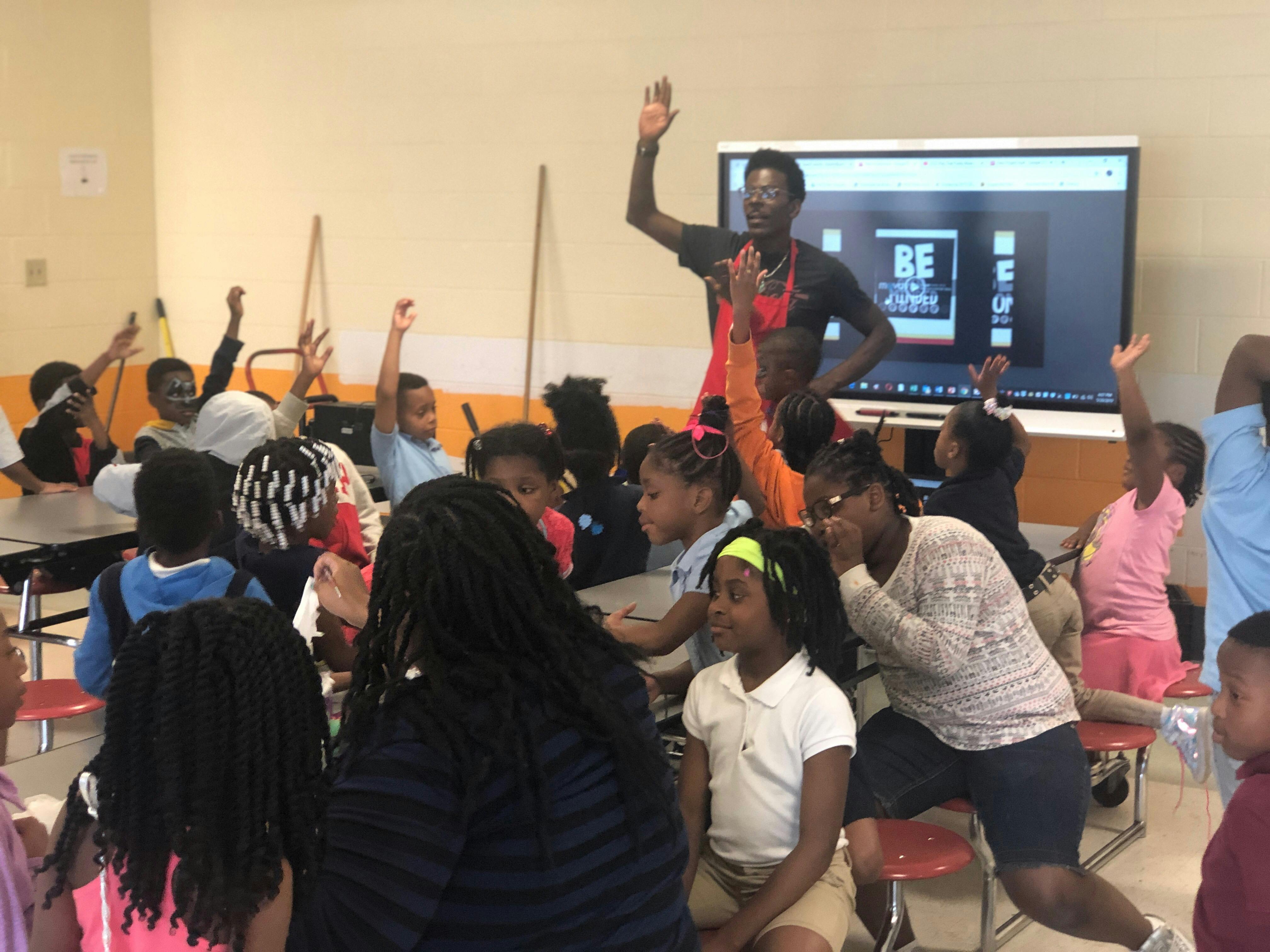 Person standing in front of children with hands raised in a classroom
