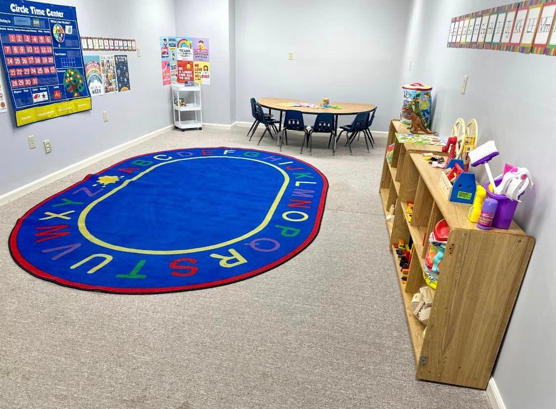 Classroom with an alphabet rug, small table and chairs, and shelves with toys