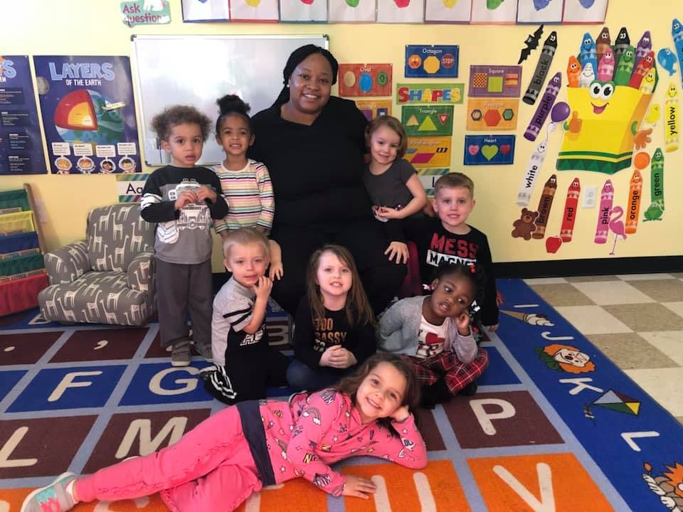 Adult and multiple children posing for a photo in a classroom