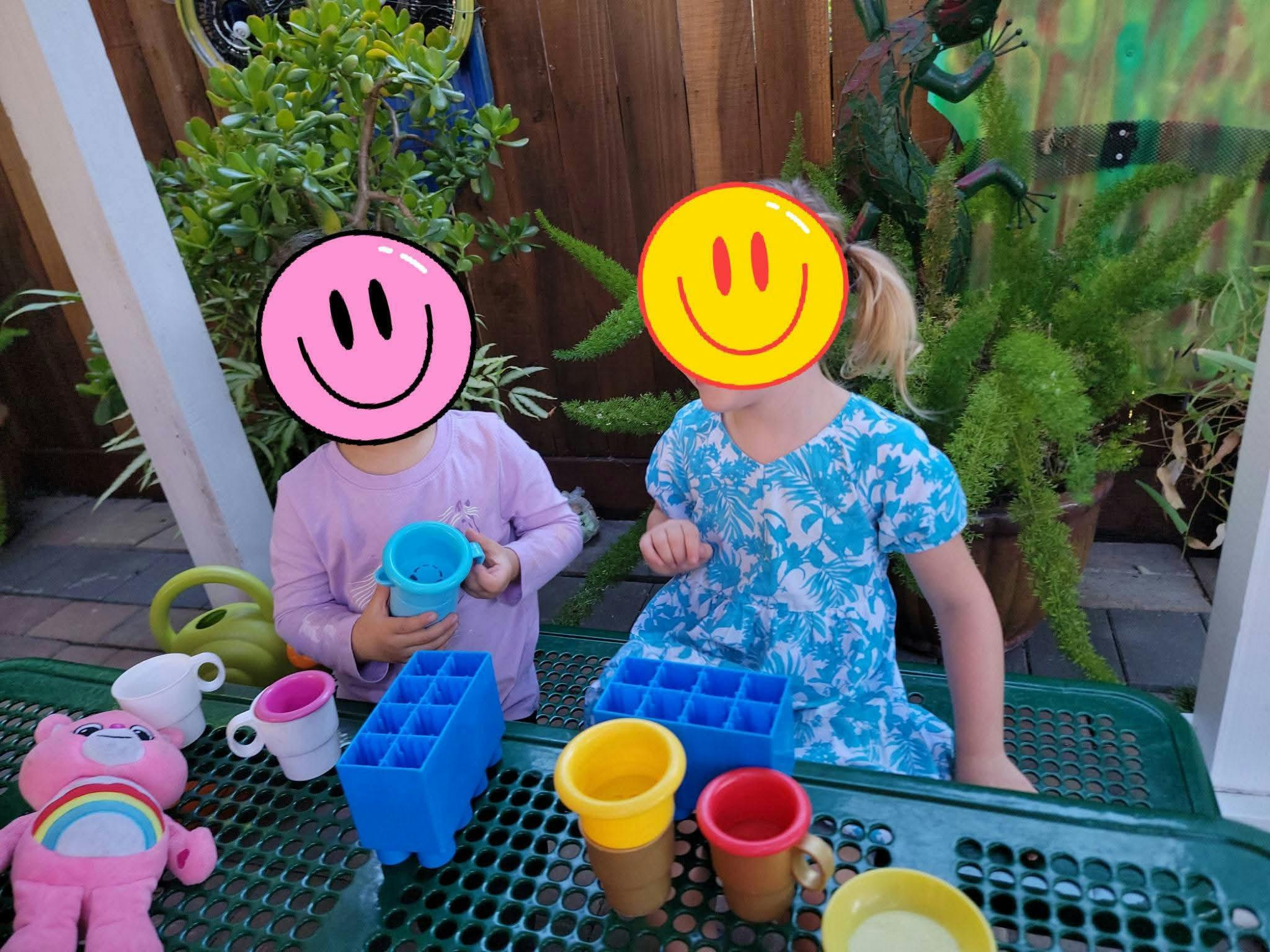 Two children sitting at a table playing with plastic toy dishes