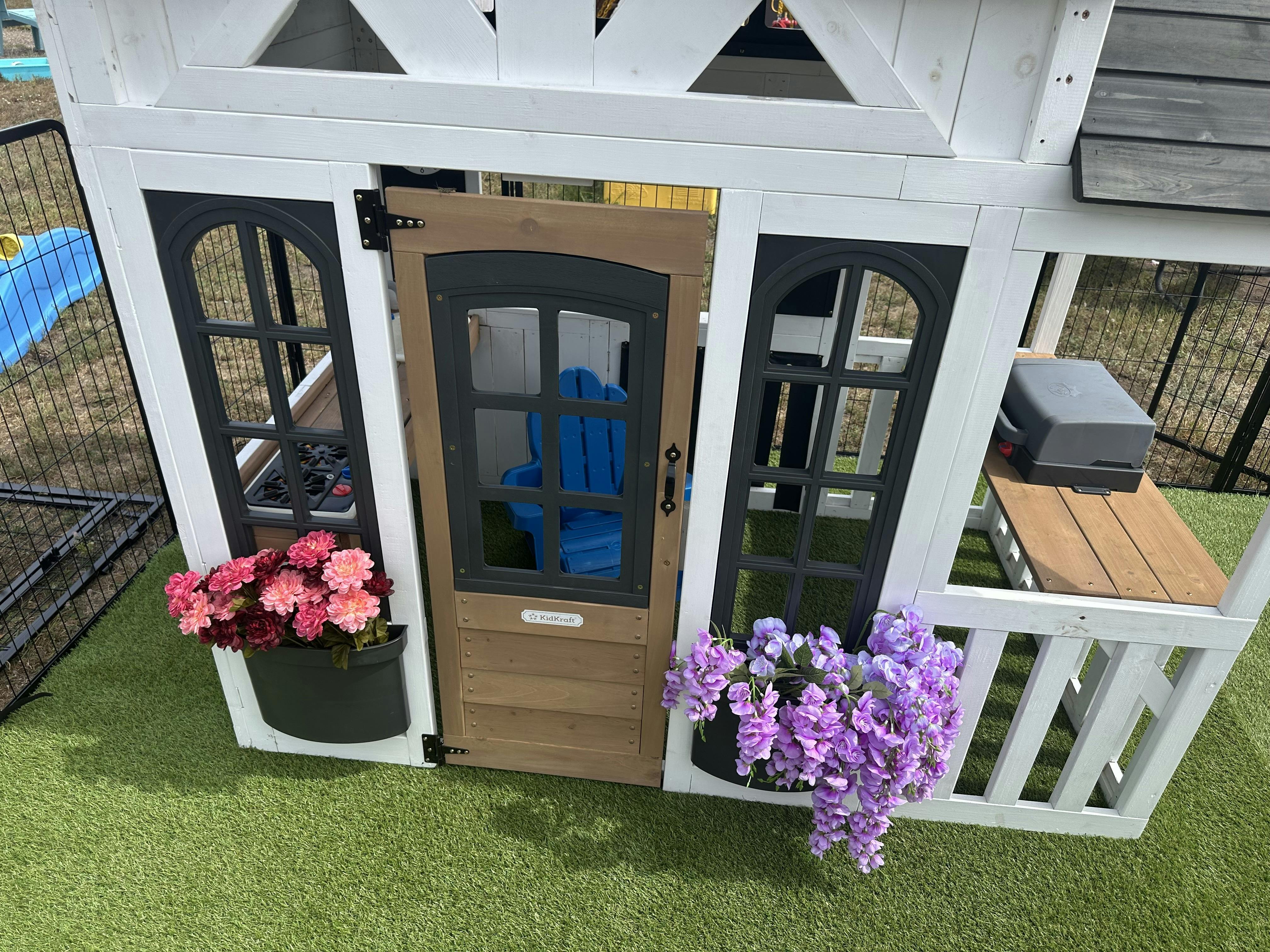 Wooden toy playhouse for children with flower boxes and a small chair inside