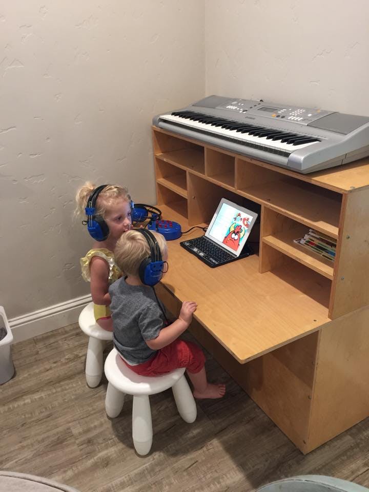 Two children wearing headphones looking at a laptop on a desk