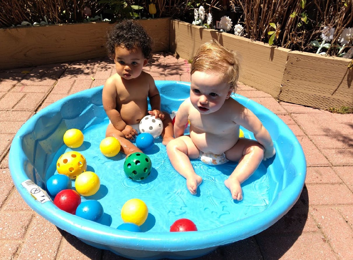 Two children sitting in a small blue pool with colorful balls