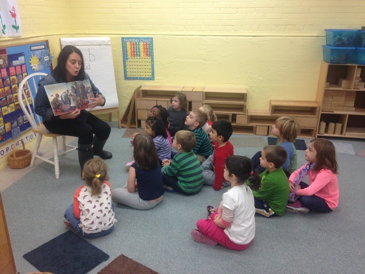 Person reading a book to a group of children in a classroom