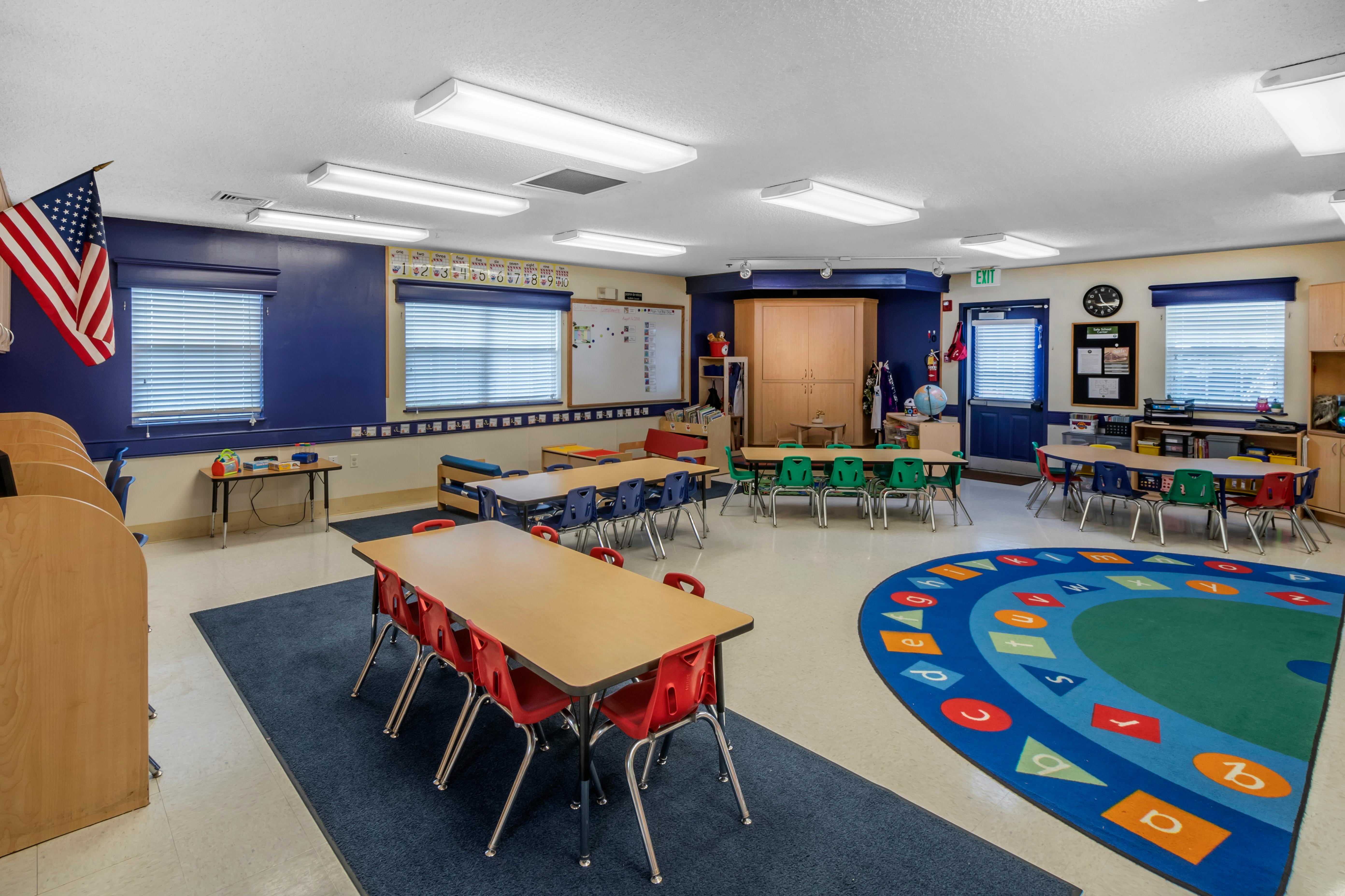 Classroom with child-sized tables and chairs, a large alphabet rug