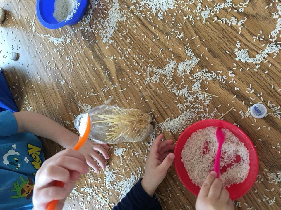Children playing with rice and small objects on a wooden floor