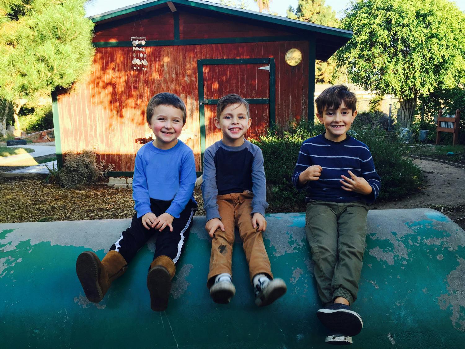 Three children sitting on a green surface in front of a wooden building