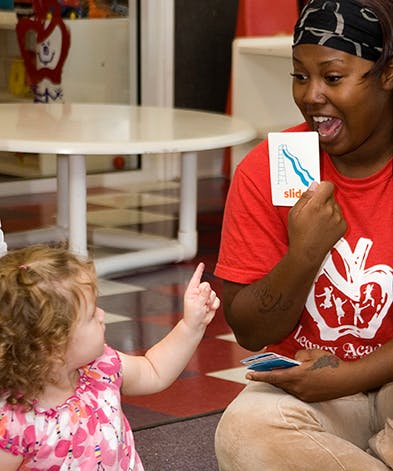 Person holding a flashcard with "slide" written on it, child pointing