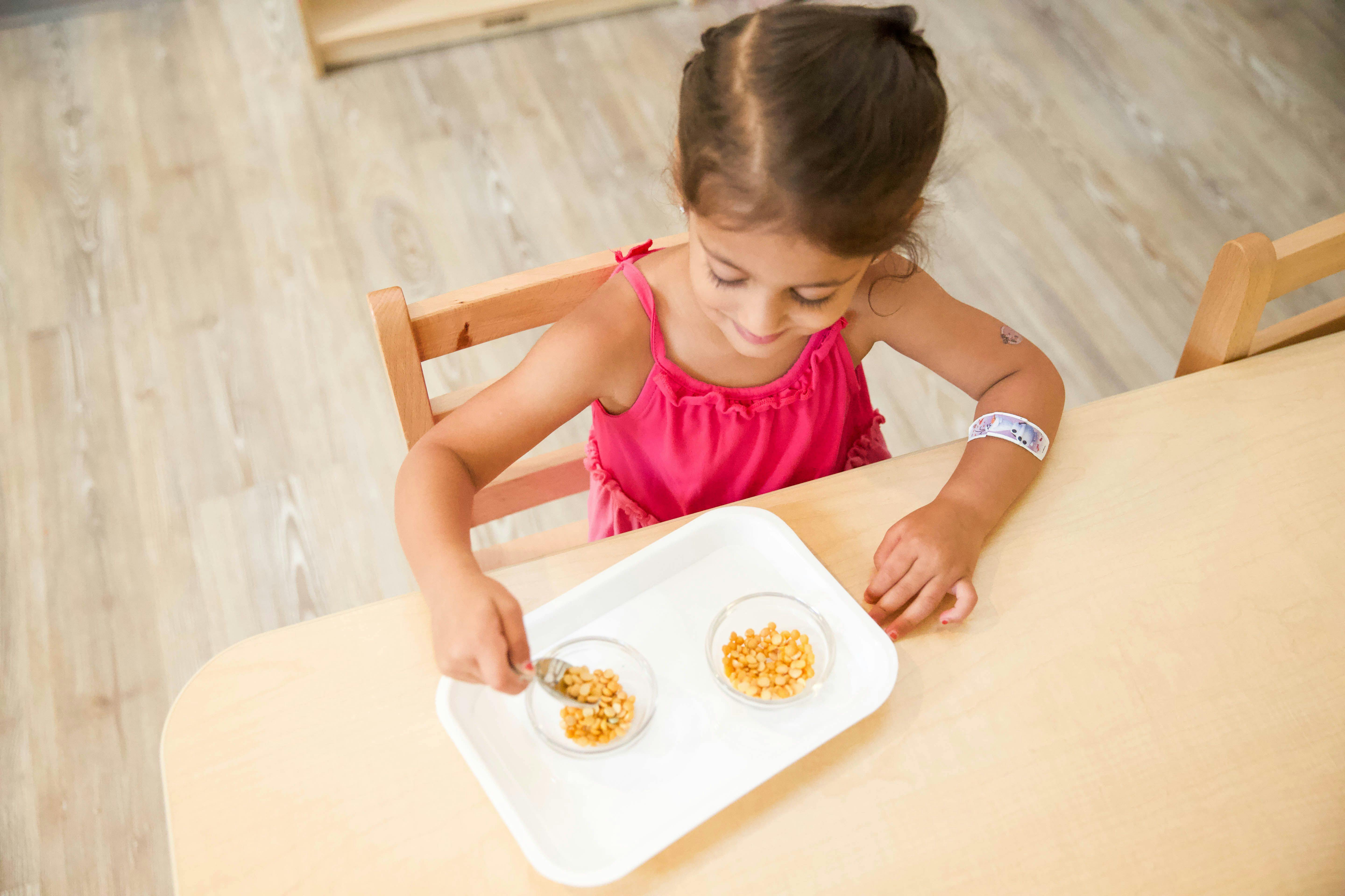 Child spooning small brown beads from one glass bowl to another