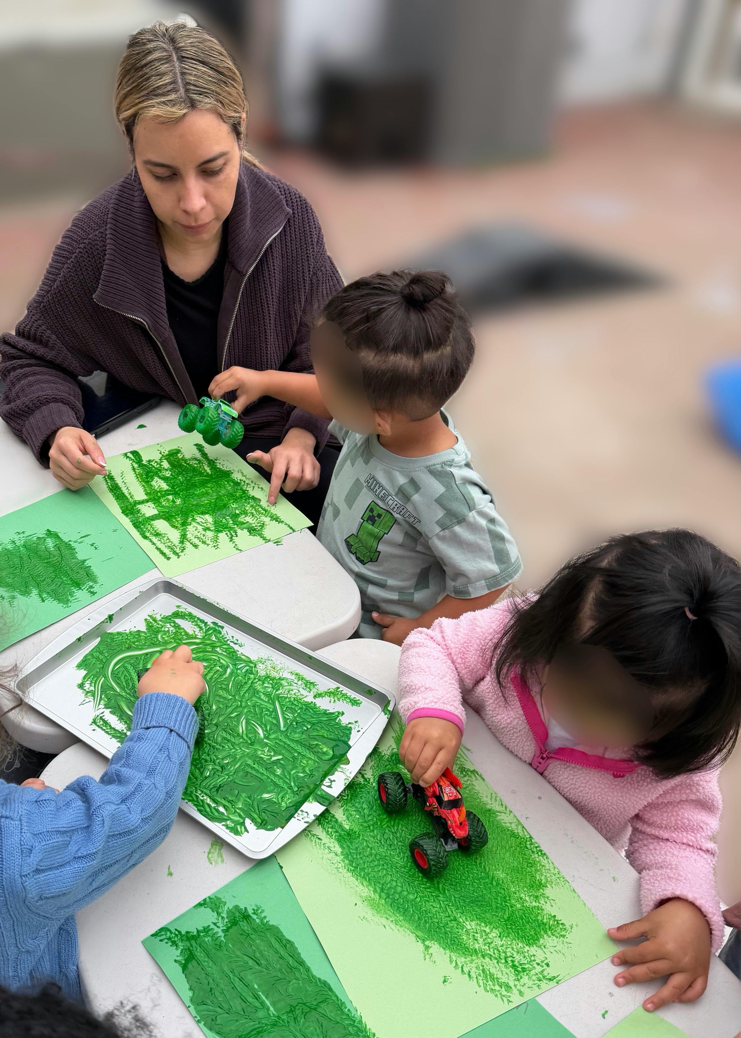 Adult and three children creating art with toy trucks and green paint
