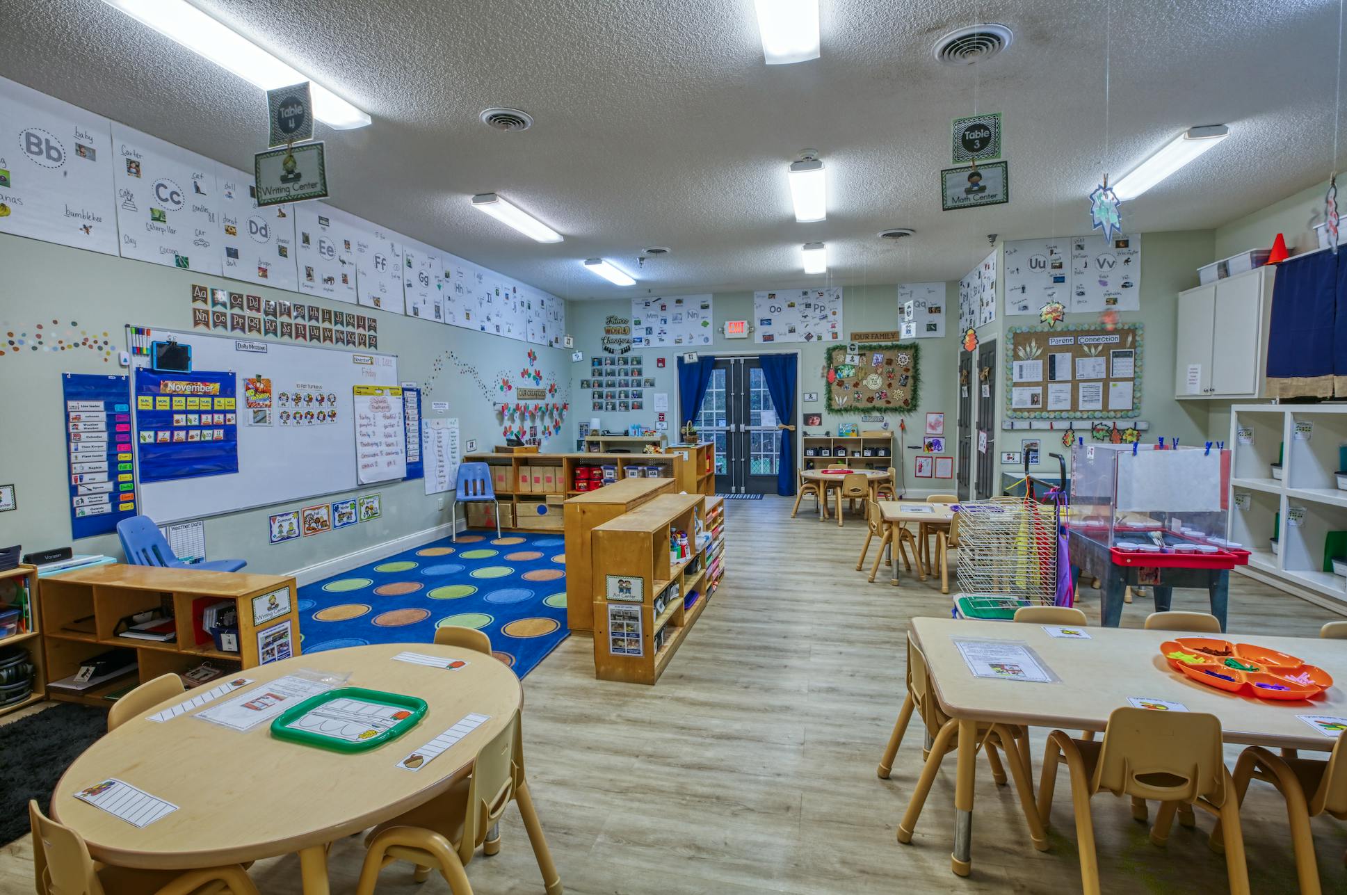Empty classroom with small tables and chairs, whiteboards, and educational posters