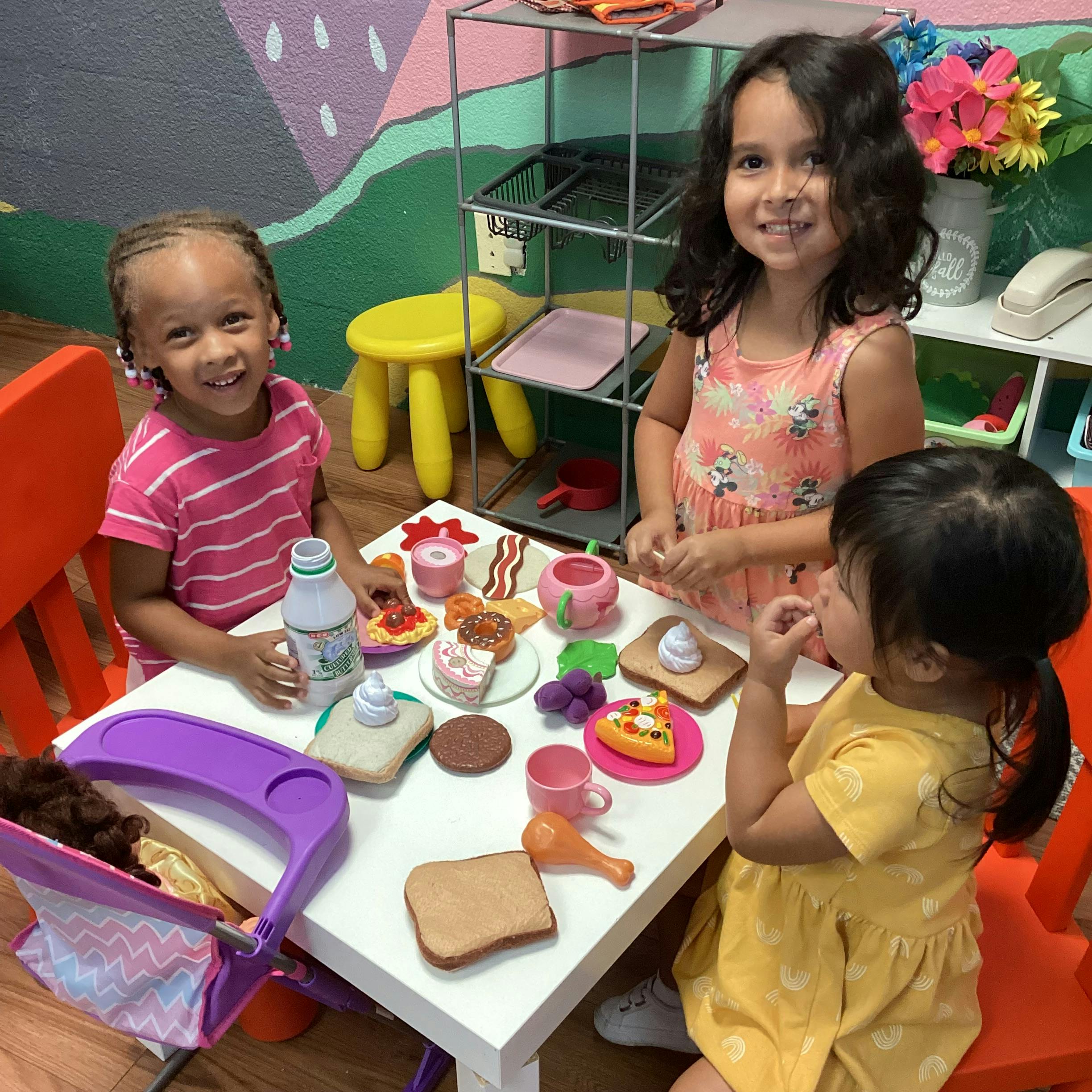 Three children playing with toy food at a small table