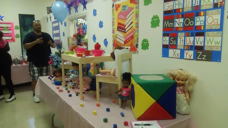 Person standing in a room with a table of toys and alphabet chart on wall