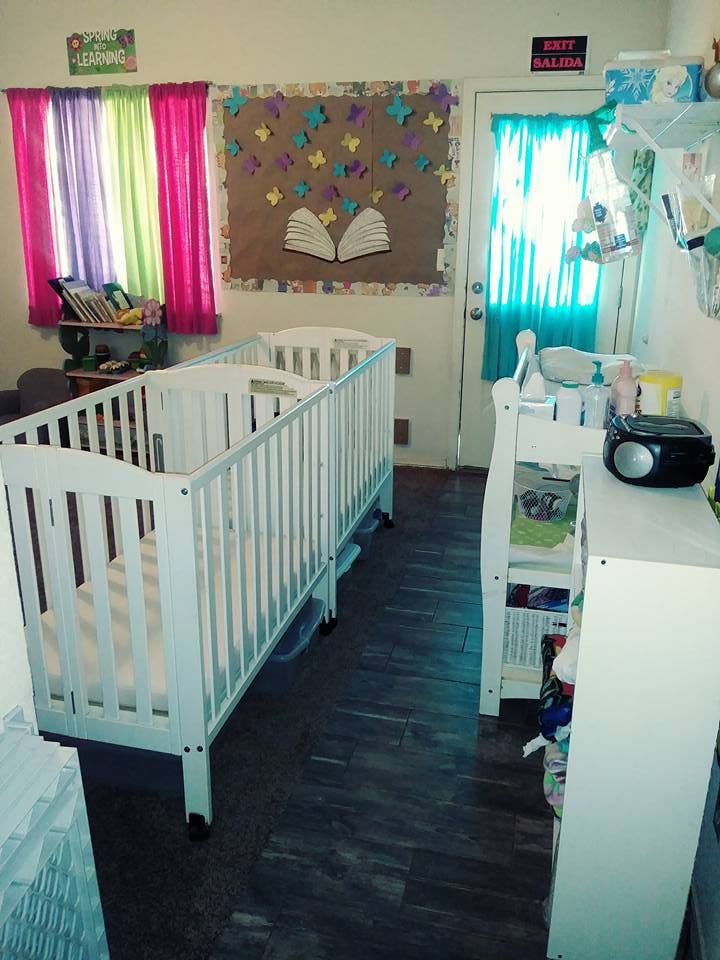 Two white cribs in a room with colorful curtains and a bulletin board
