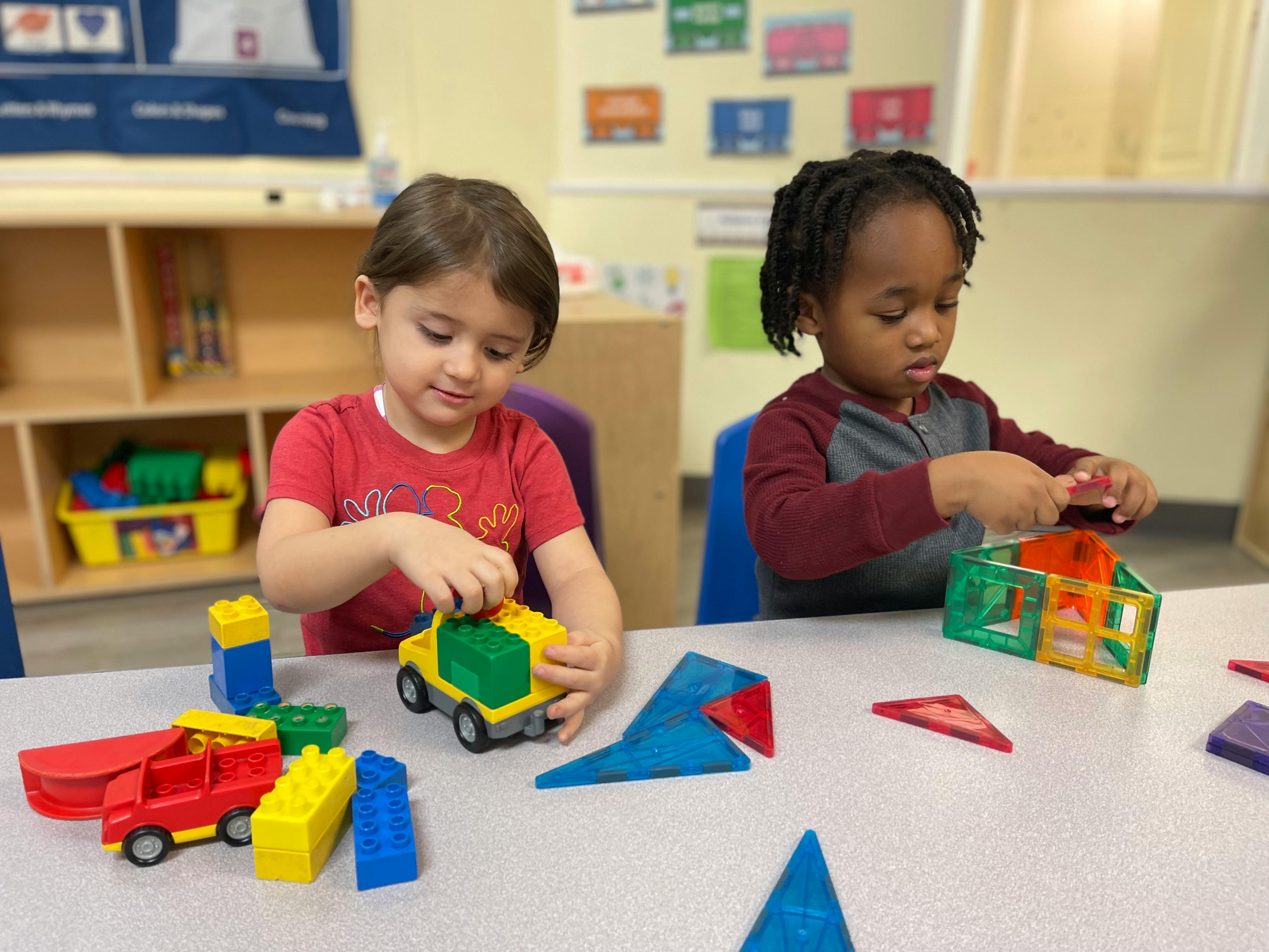 Two children playing with toys at a table in a classroom