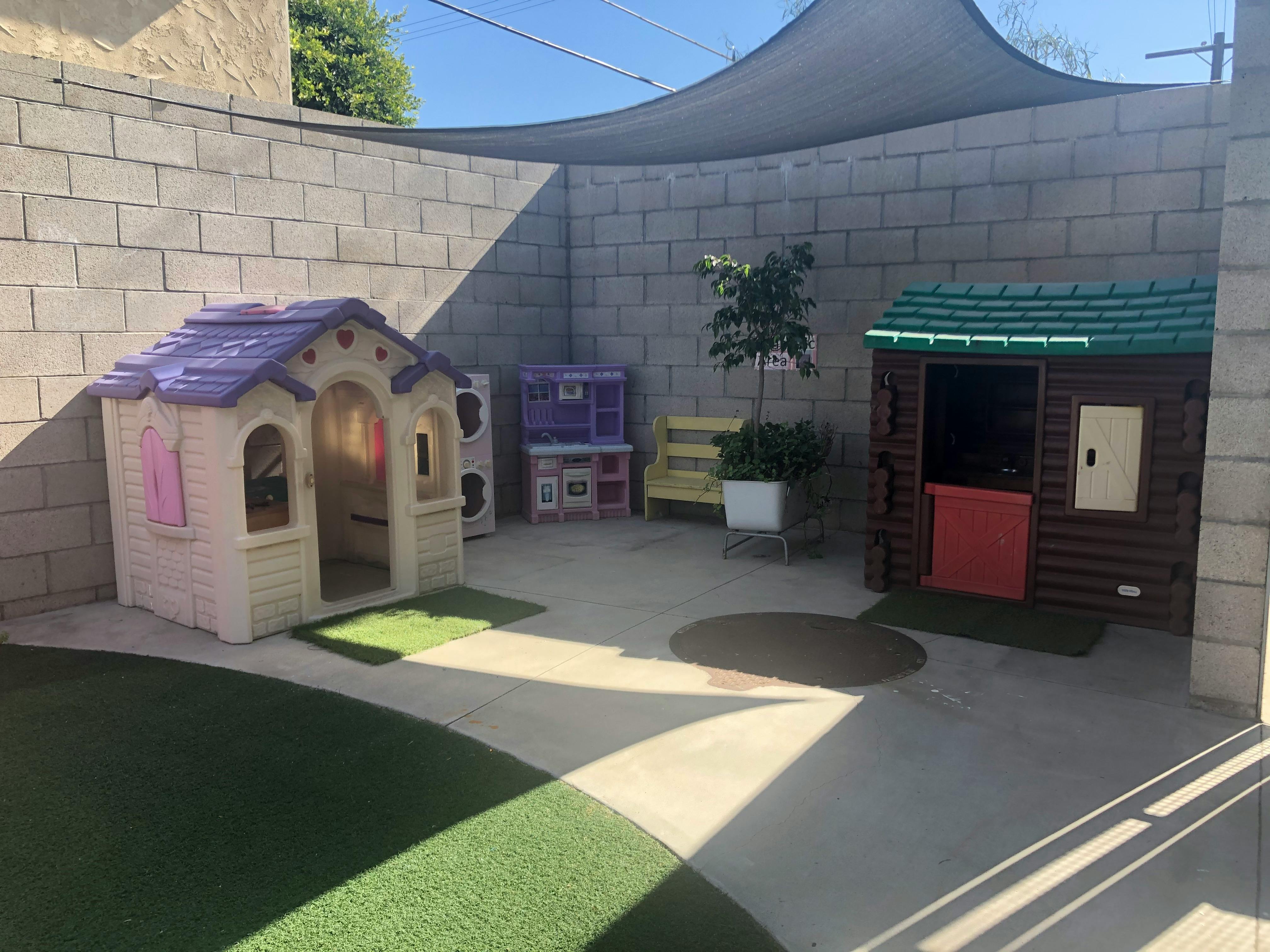 Two playhouses in an outdoor area with a concrete wall and shade