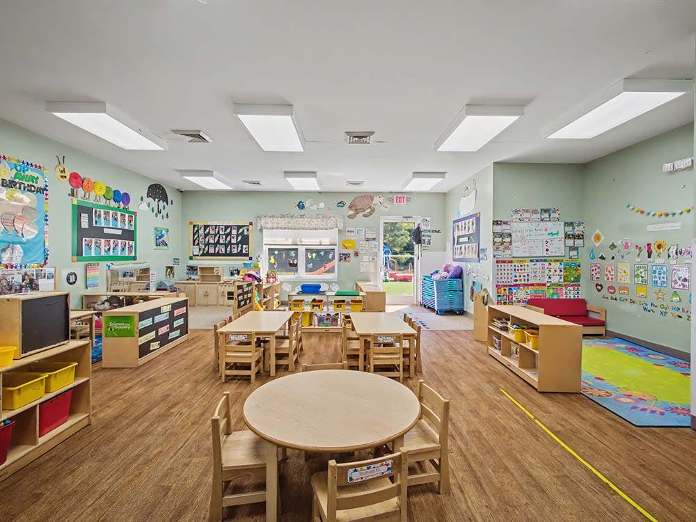 Empty classroom with small wooden tables and chairs, shelves, and wall decorations