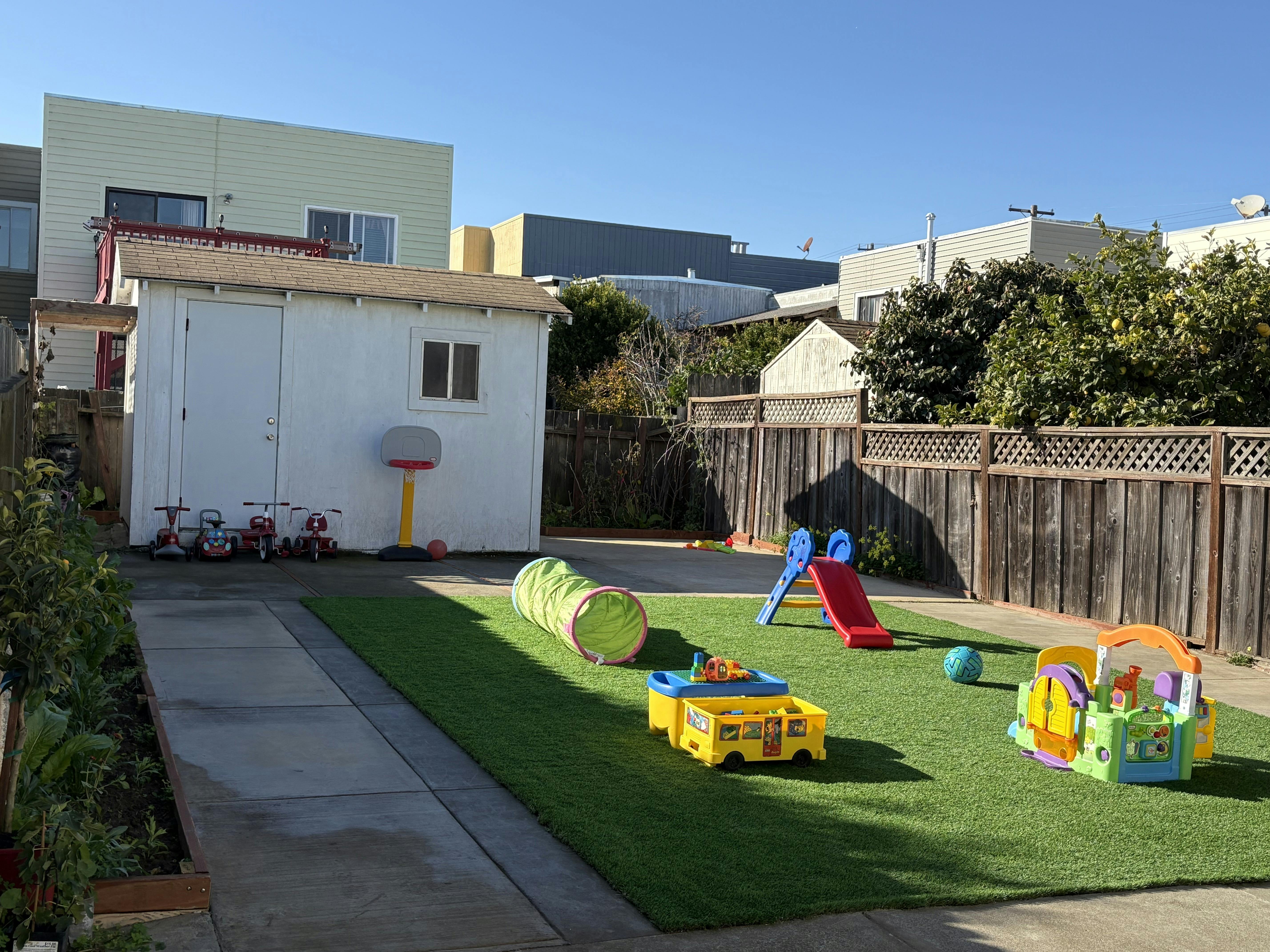 Outdoor play area with artificial turf, slide, tunnel, and toys