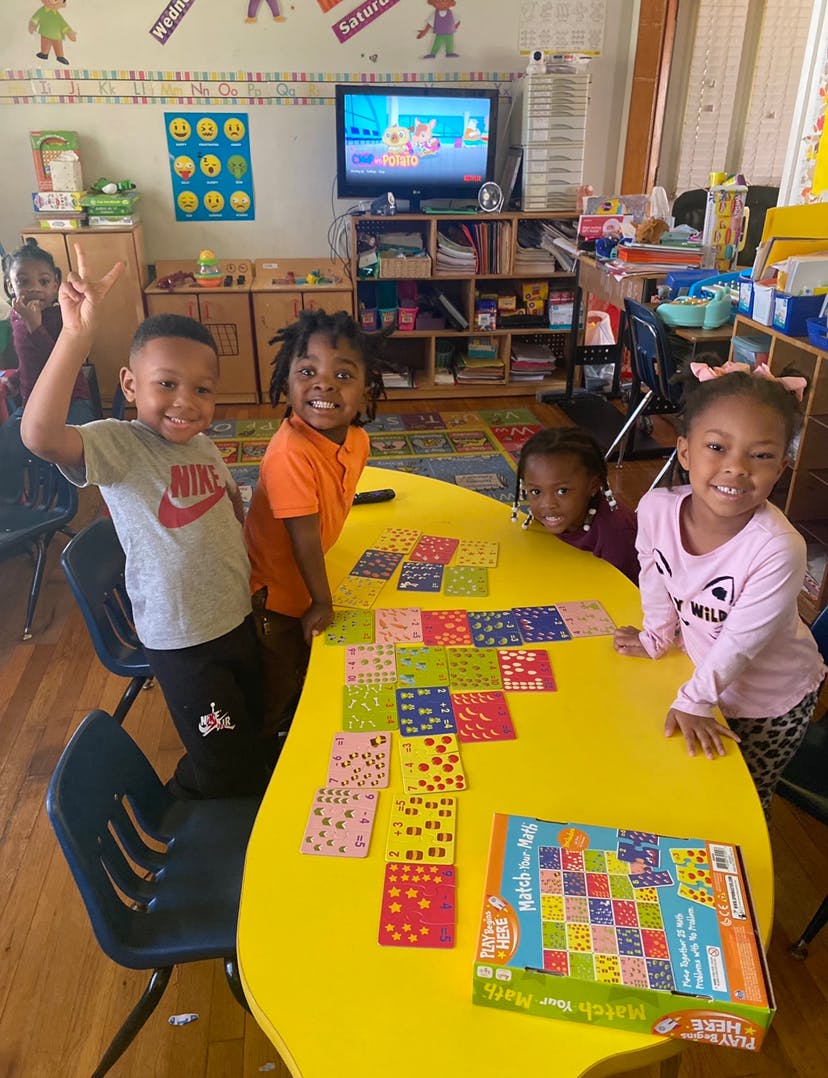 Four children playing a game at a yellow table in a classroom