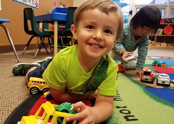 Child playing with toy cars on a rug in a classroom