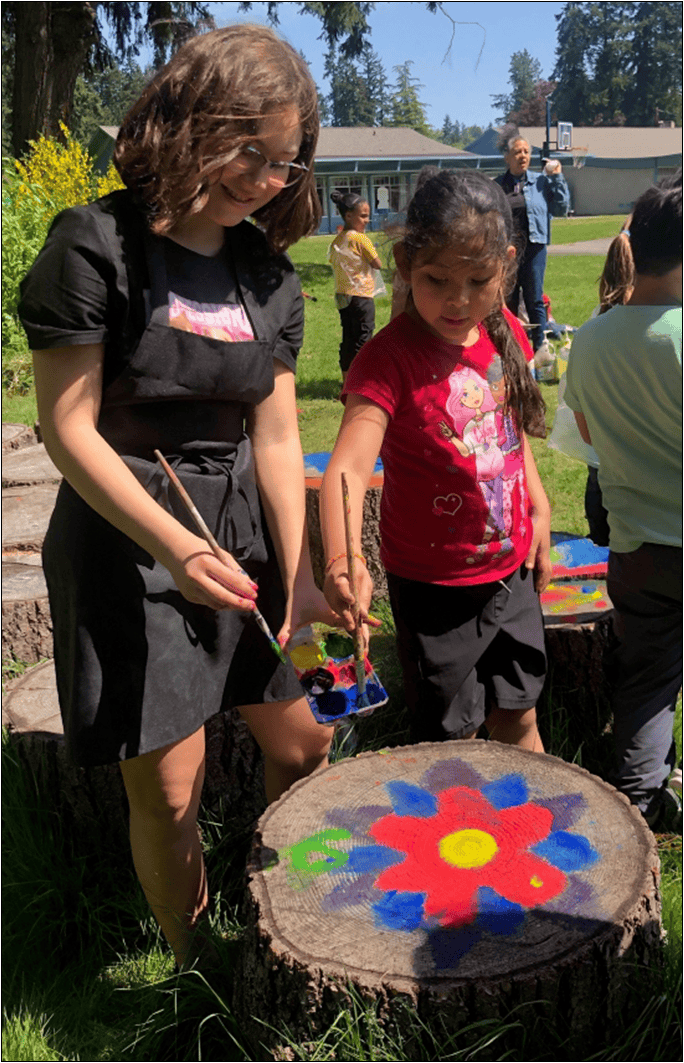 Person and child painting a flower design on a tree stump outdoors