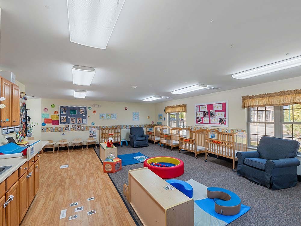 A daycare room with cribs, chairs, and play equipment