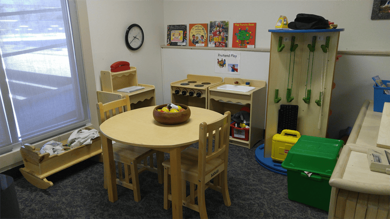 Children's play area with small table and chairs, toy kitchen, and shelves