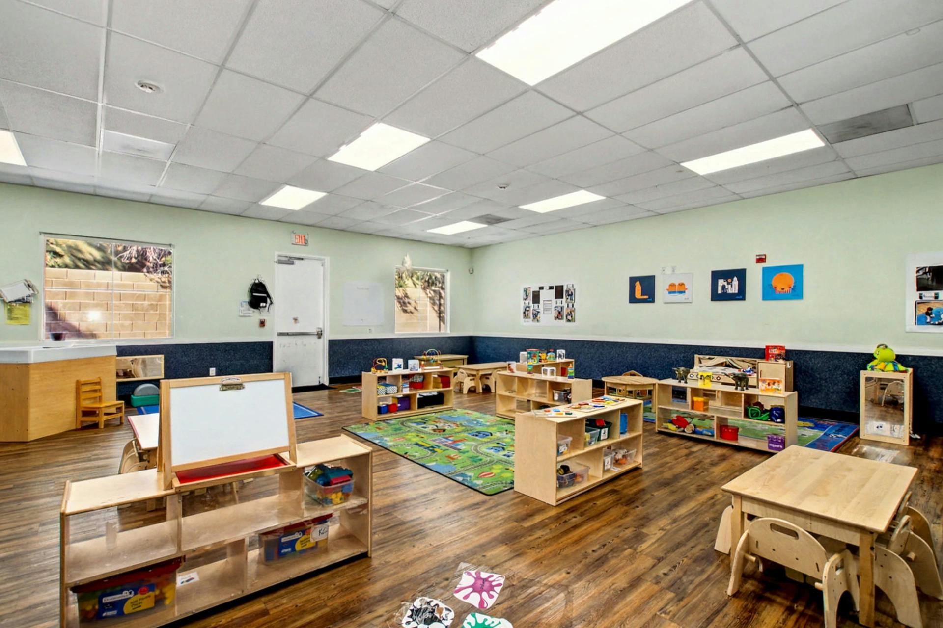 A classroom with wooden furniture, toys, and a colorful rug