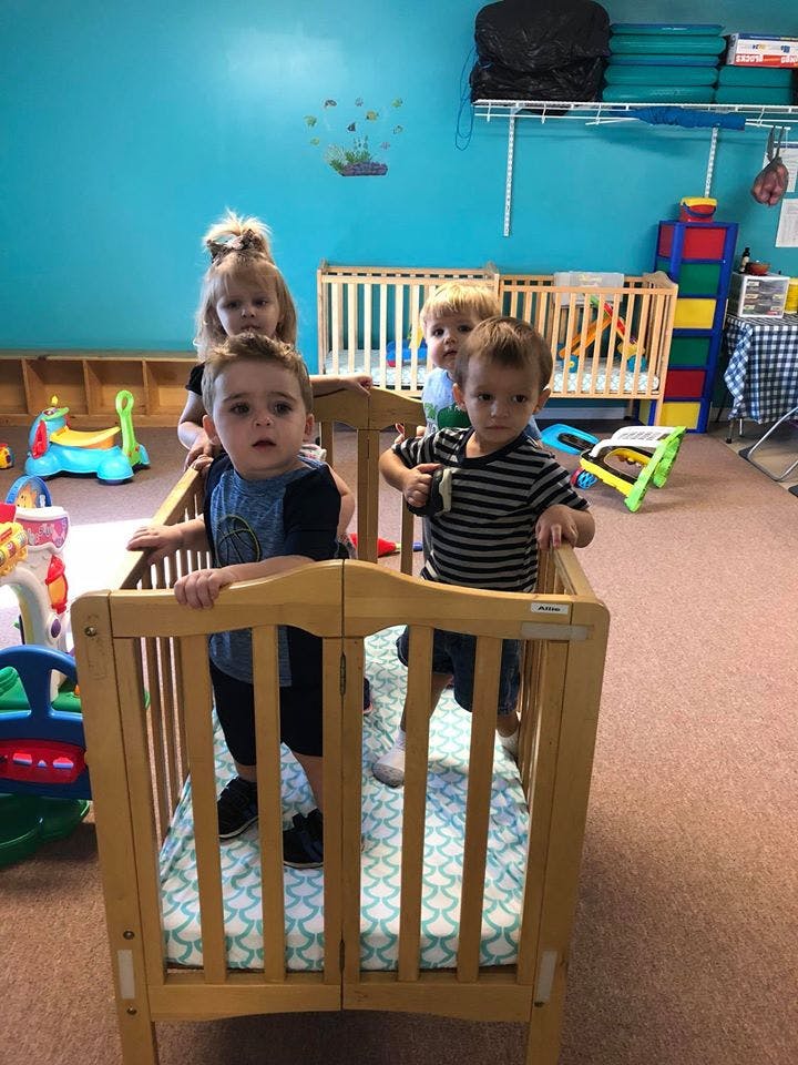 Four children standing in and around cribs in a room