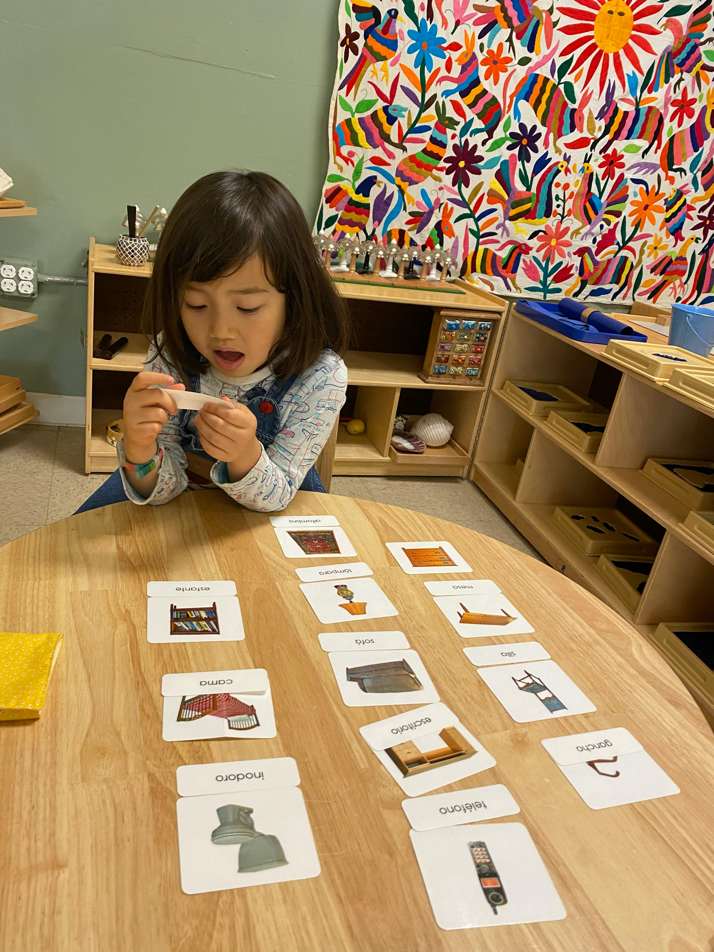 Child holding a small card at a table with other cards spread out
