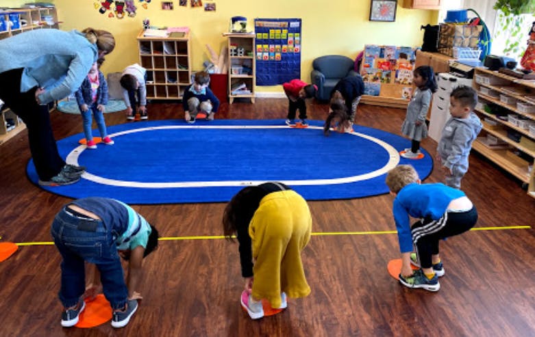 Adults and children playing with orange cones on a wooden floor in a classroom