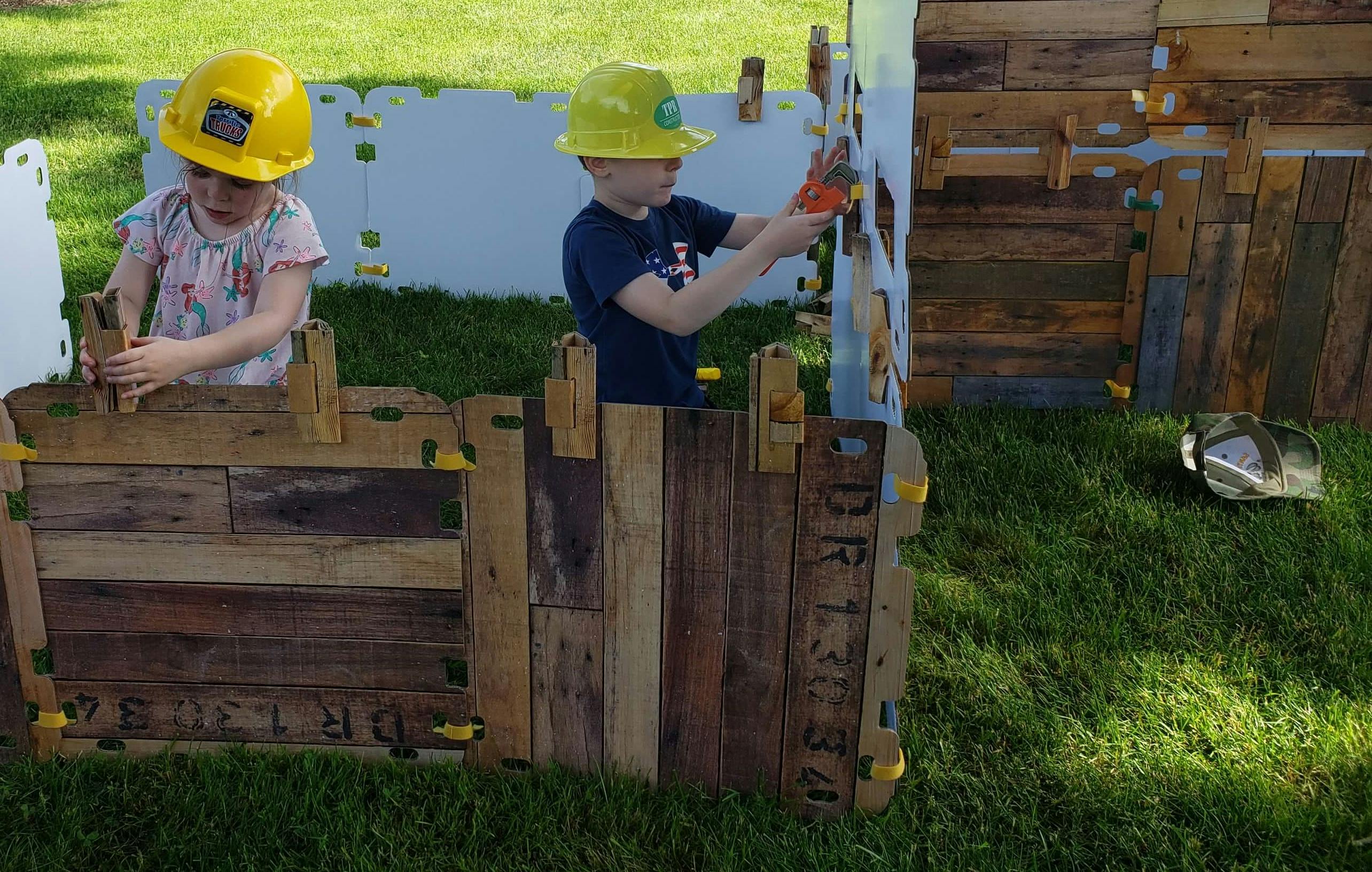 Two children in hard hats playing with wooden blocks outdoors