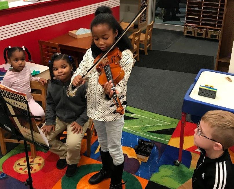 Child playing a violin for other children