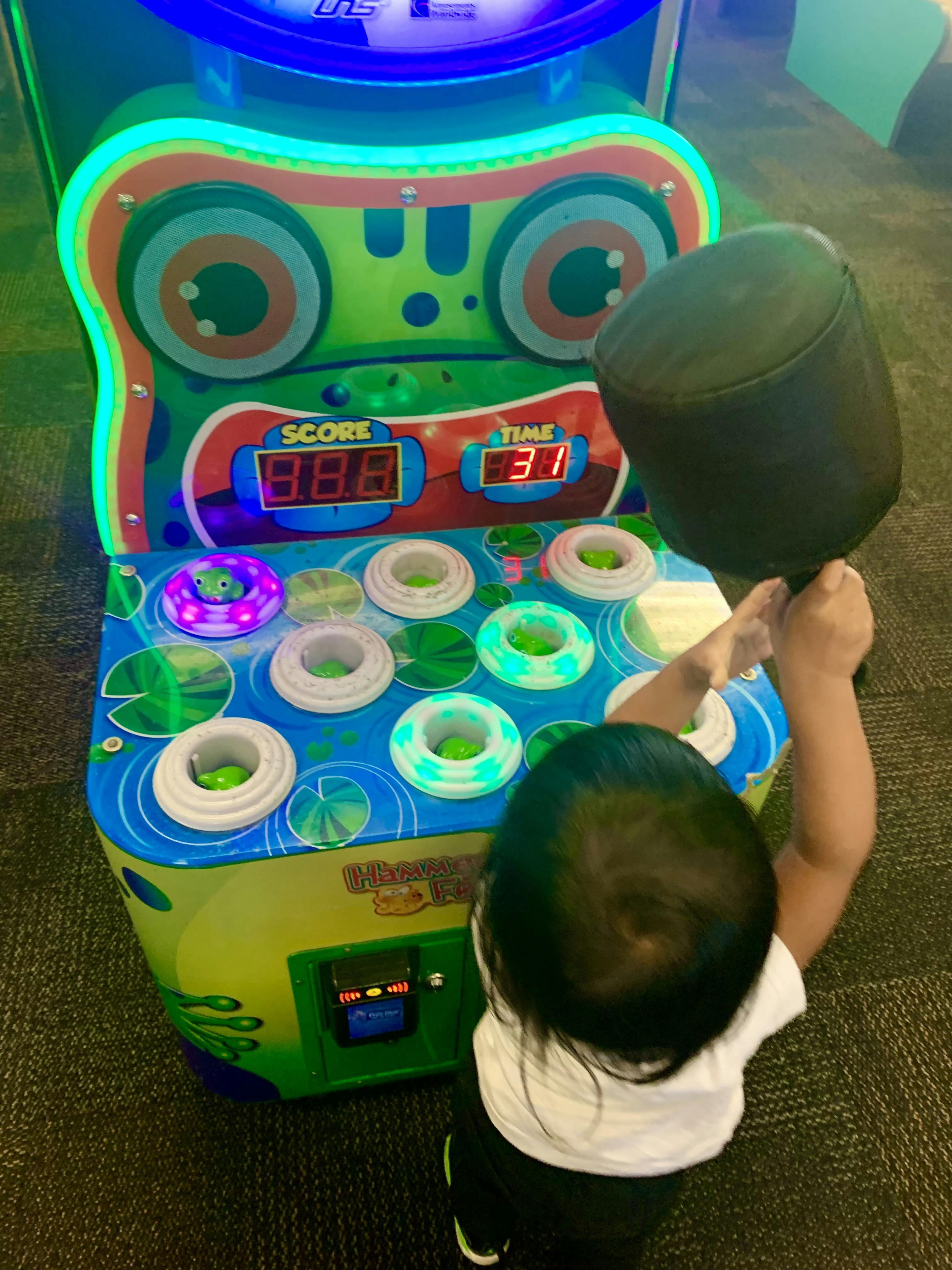 Child playing a whack-a-frog arcade game with a mallet