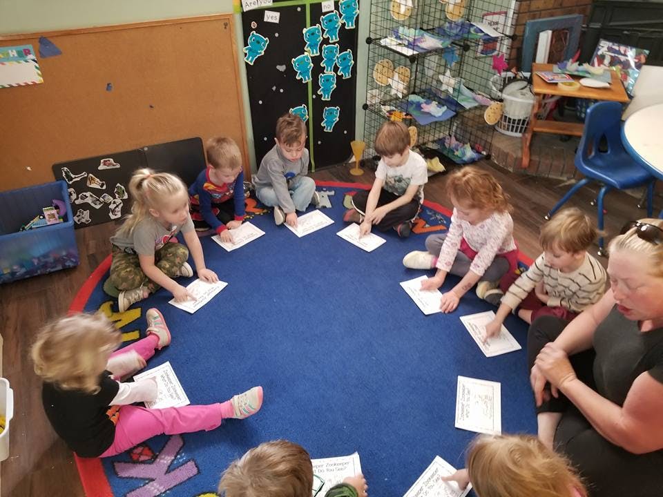 Children and an adult sitting in a circle on a rug with papers