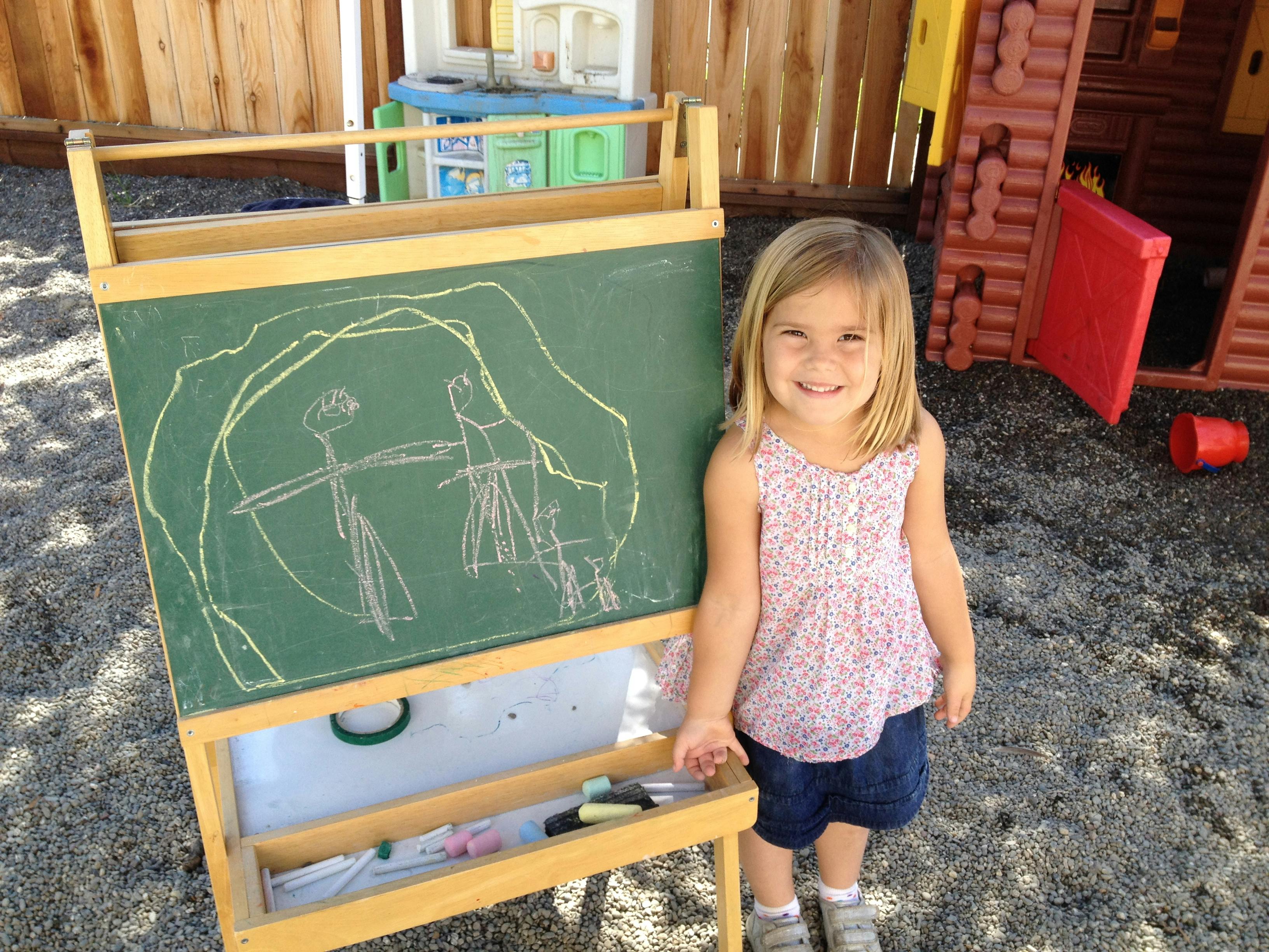 Child standing next to a chalkboard with drawings