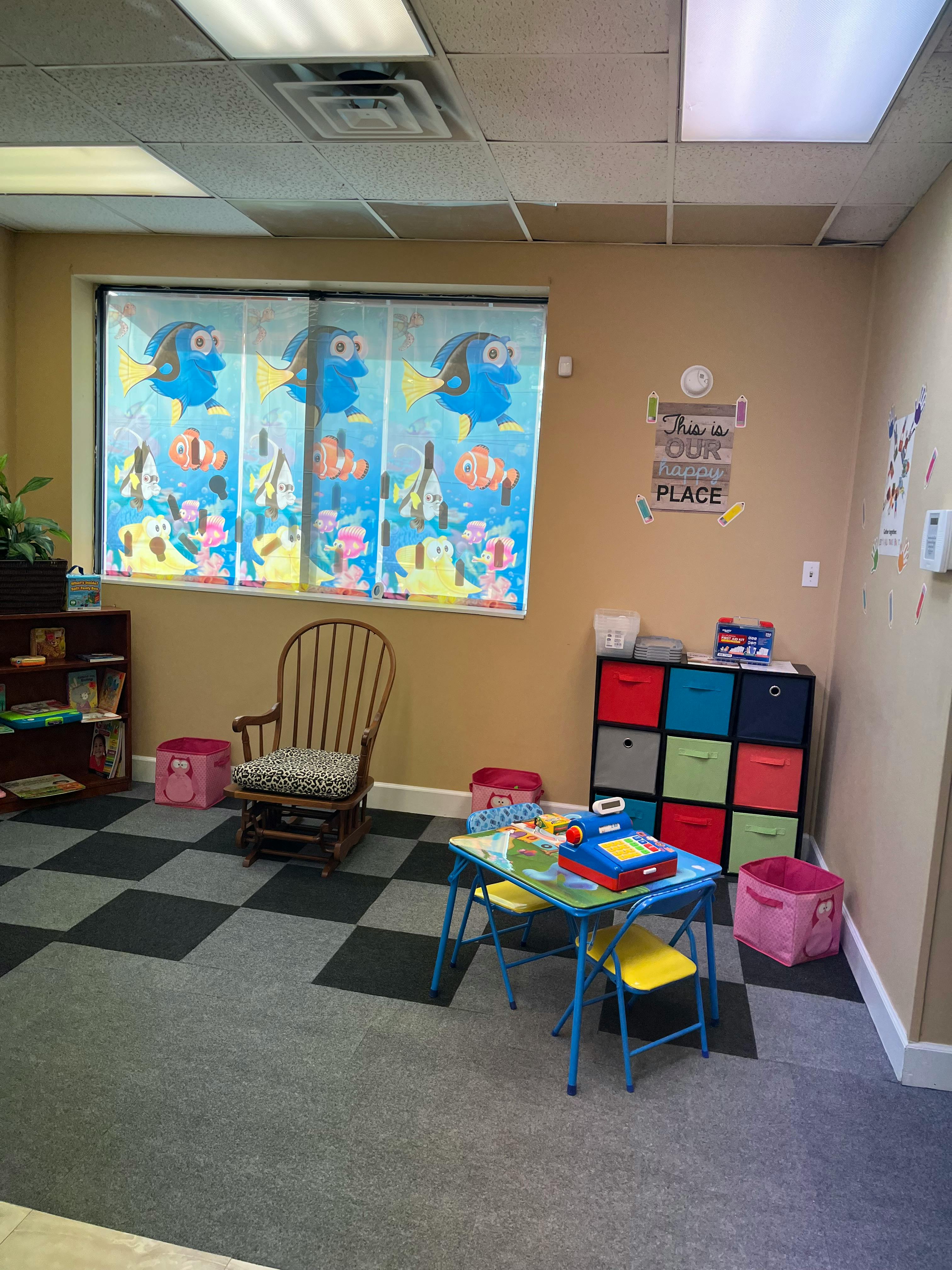 Children's play area with small table and chairs, storage unit, and window with cartoon fish