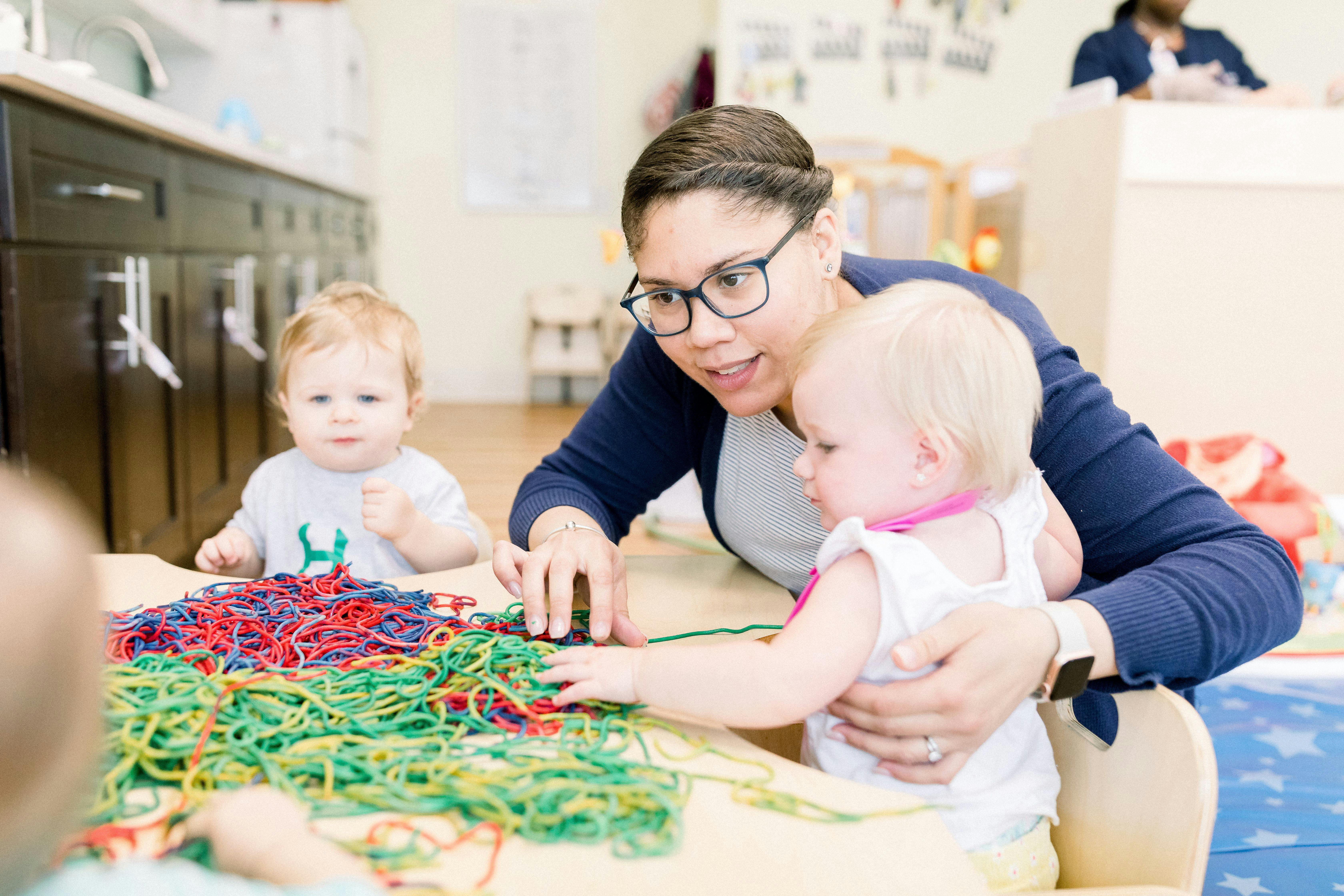 Person in glasses helping two children play with colorful string