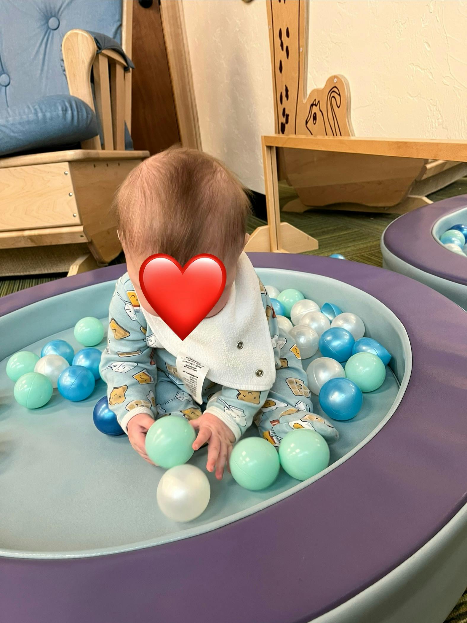 Child sitting in a small ball pit playing with plastic balls