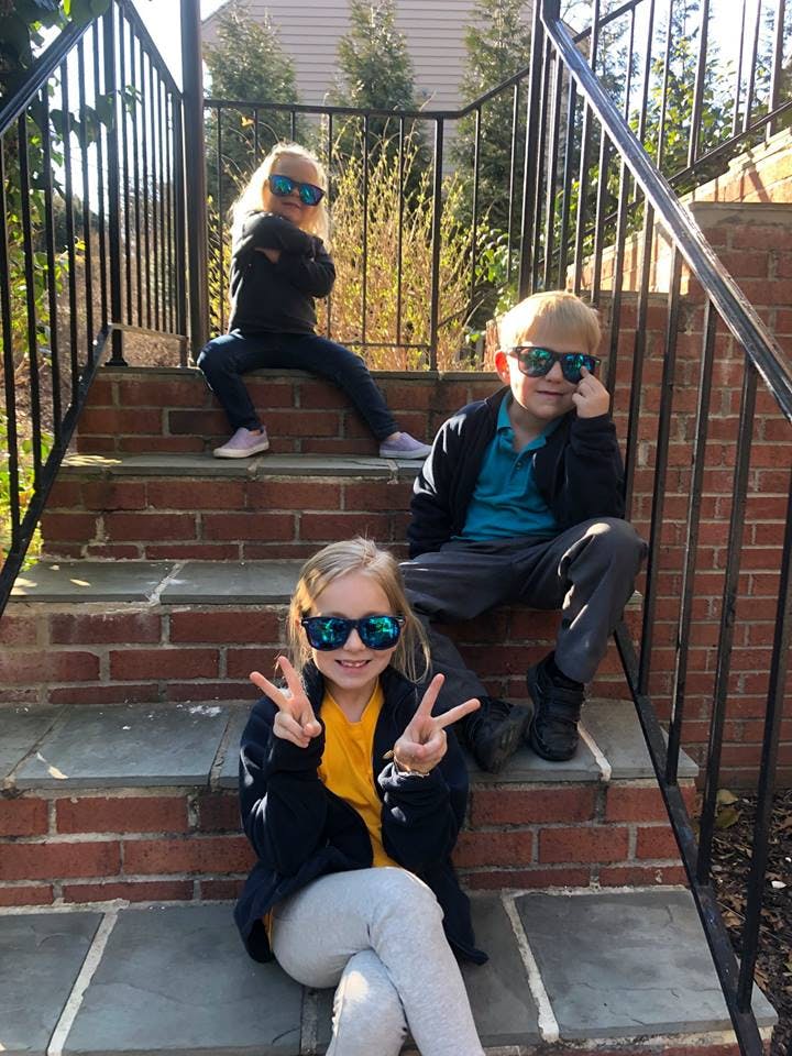 Three children wearing sunglasses sitting on brick steps