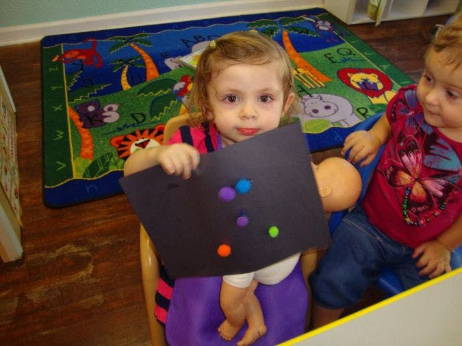 Child holding black paper with colorful pom-poms