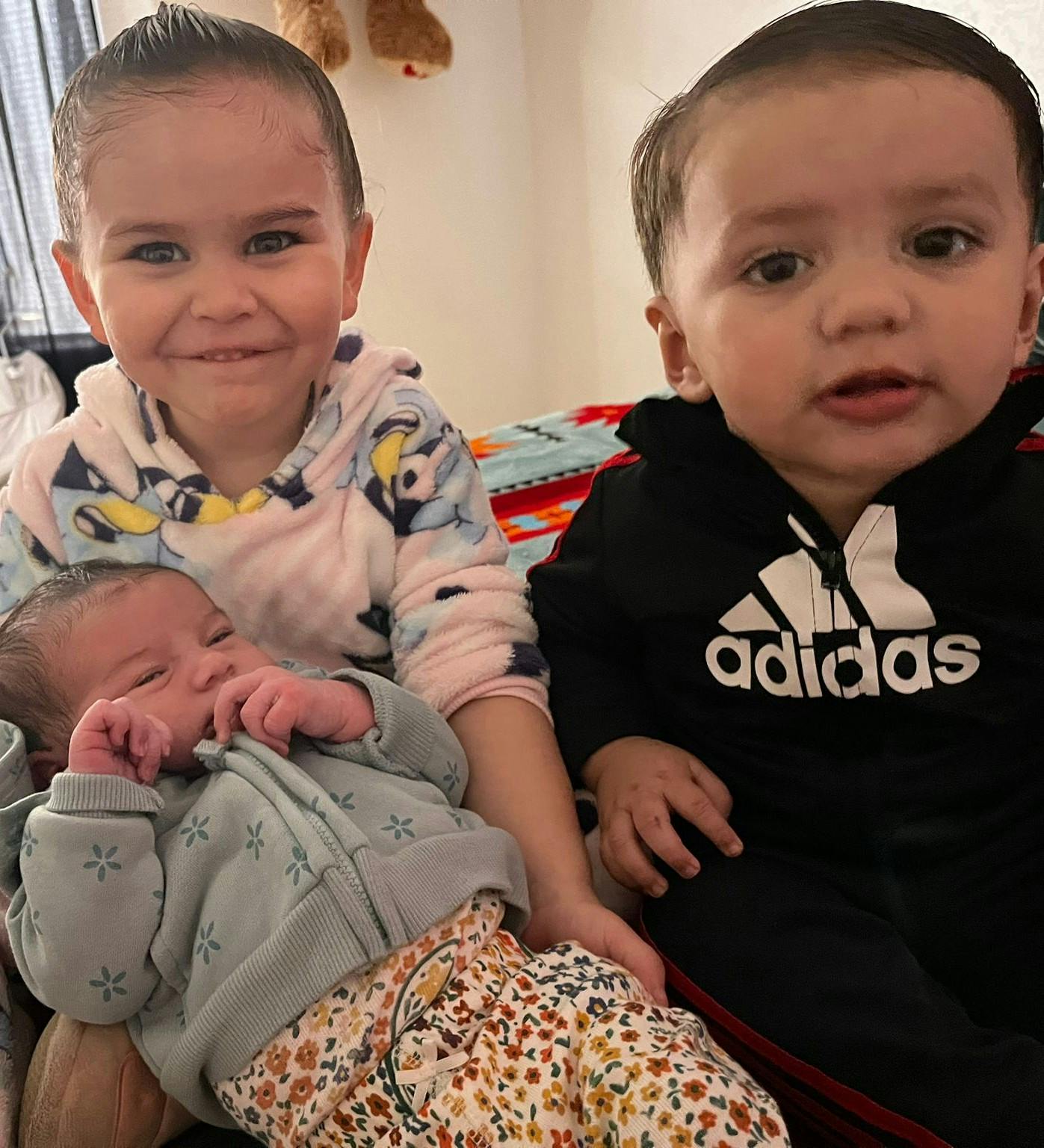 Three children sitting together, one smiling, one looking forward, one sleeping