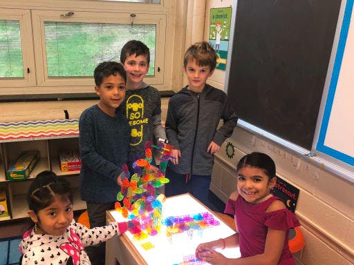 Five children around a light table with colorful building blocks