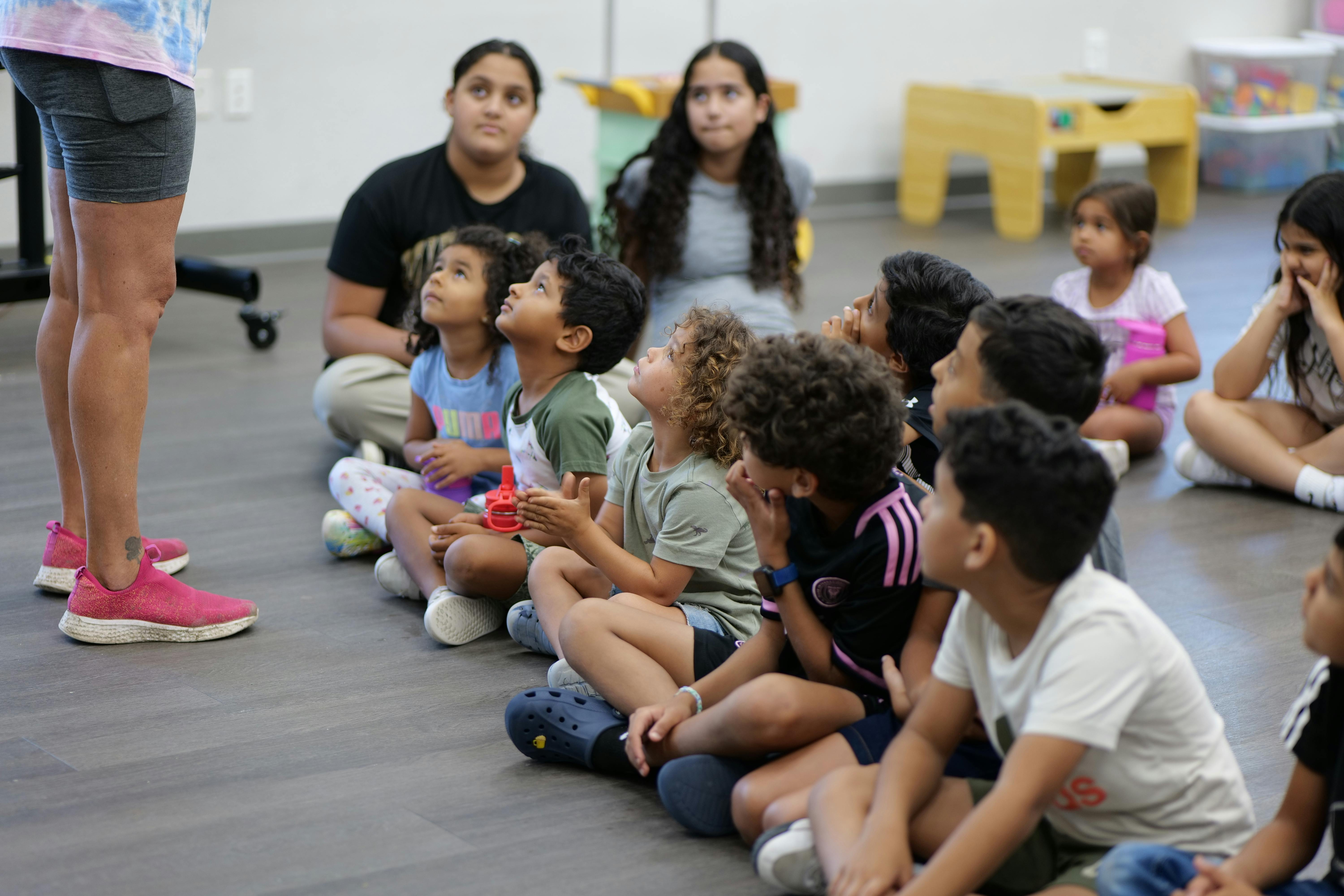 Children and adults sitting on the floor looking up at a person standing