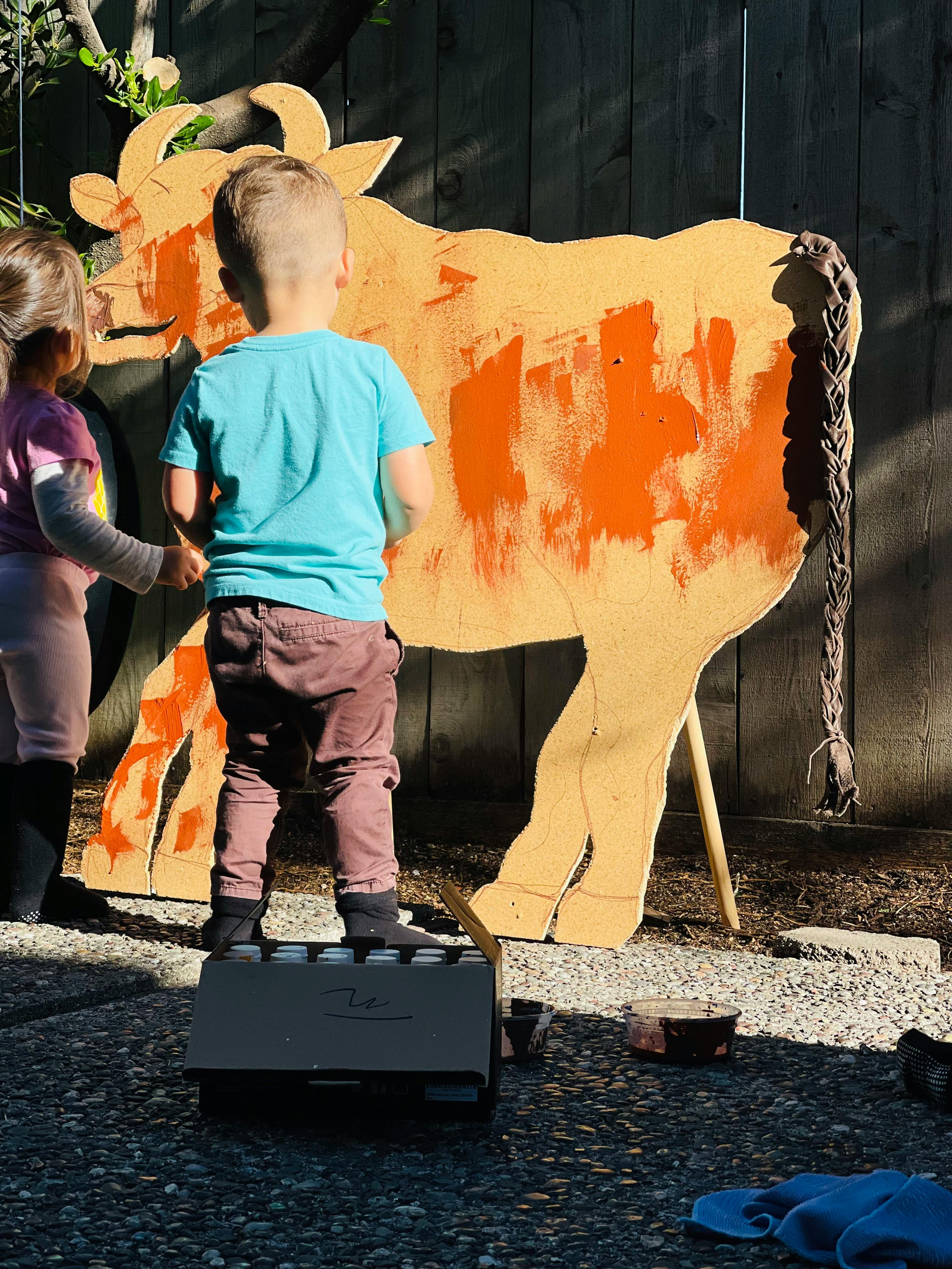 Two children painting a large wooden cow cutout