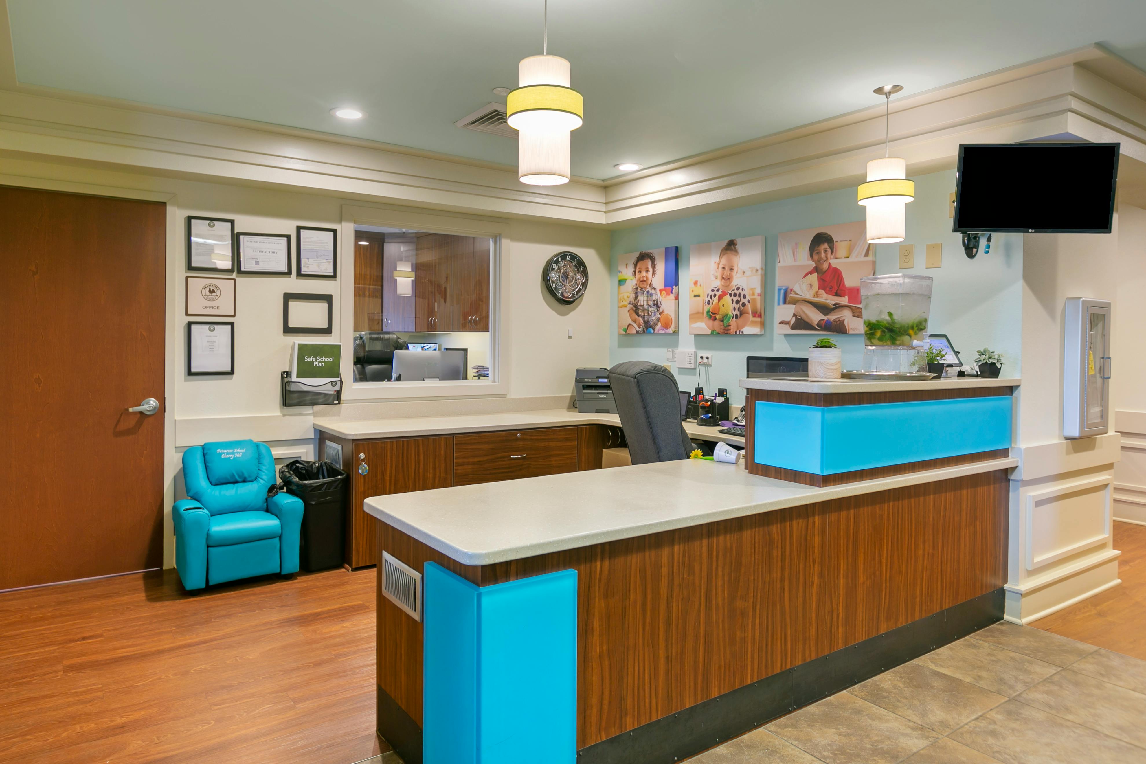 Reception area with a light brown desk, blue chair, and photos of children