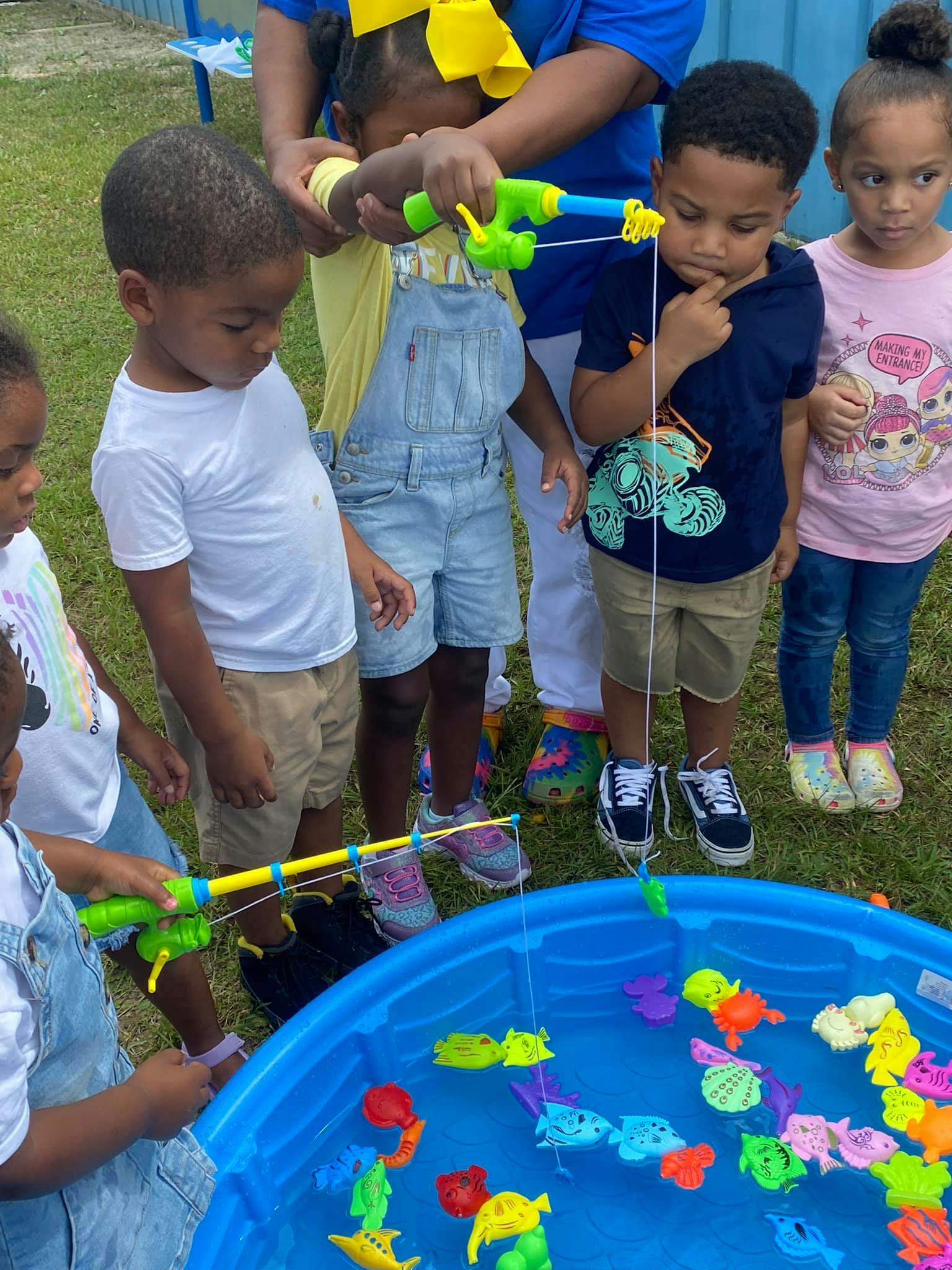 Children playing a fishing game with toy rods and plastic fish in a blue pool
